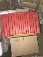 15 red hardcover volumes of Britannica Junior Encyclopedia arranged side by side, showing spines with gold embossed lettering.