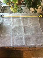 Photo of a plain, very sheer scarf spread flat with a measuring tape showing about 26 inches across, placed on a kitchen counter with plants in background.