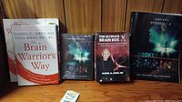 Four brain-related items on a wooden shelf: Two books and two DVD boxed sets.