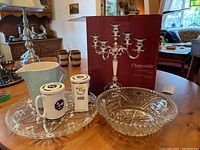 Shot of all items in the lot showing candelabra, serving platter, crystal bowl, and mugs on a table inside a living room.