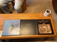 Three vinyl record covers on a wooden coffee table showing Eagles and Crosby, Stills, Nash & Young albums.