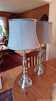 Pair of matching lamps on wood table with white shades shown in a living room setting.