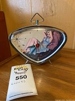 Front angled view of triangular Marilyn Monroe alarm clock on wooden surface with auction tag showing measurements