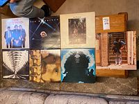 Seven vinyl record albums laid out on a table and carpeted floor. Albums include works by Van Morrison and Bob Dylan, showing front covers.