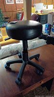 Side view of the rolling stool showing the black padded seat and five caster wheels.