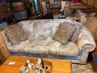 Full front view of the three-seat sofa with patterned fabric upholstery and two decorative floral cushions, placed in a basement room.