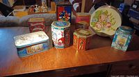 Full view of the assorted decorated storage tins displayed on wooden surface showing different designs and shapes.