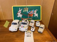 Toy cars with visible stains and the White Rabbit vintage tin box in the background.
