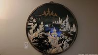 Front view of the round black lacquer wall art showing scenic inlaid shell pieces of pagodas, mountains, and trees