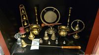 Full view of assortment showing various brass items including gong, tri-bell stand, candle holders, and decorative bowls and bells.