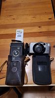 Two vintage cameras on a wood table: Kodak Brownie in leather case and Canon PowerShot with case.