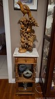 Full view of the carved wood sculpture mounted on marble-topped wooden stand
