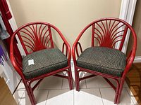 Pair of red bentwood chairs with curved backrests featuring a fan design and black/white cushions, placed on tiled floor near wall.