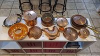 Overview of all copper cookware pieces and molds on a white table