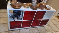 Front view showing white shelving unit with five red baskets and copper cookware on top