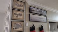 Photo showing two framed horizontal landscape prints above a doorway, featuring calm water scenes with reflections and boats.