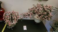 Two glass bonsai trees with pink blossoms on a black table, one large and one smaller, both in ceramic pots.