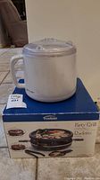 Oster ice cream maker placed on top of the Trudeau Party Grill box, showing the ice cream maker unit and box with product image and description.