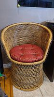 Full view of the rattan chair showing woven design and red cushion.