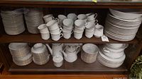 Shelved display showing stacks of plates, cups, sugar bowl and creamer in china cabinet
