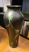 Full view of tall pottery vase with hand painted green and orange design on black matte base