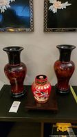 Two matching painted wood vases and Chinese corked bottle displayed on a black table under framed floral artwork.