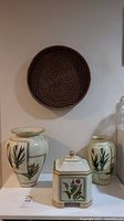 Full front view showing two pottery vases, square lidded jar, and the round woven basket mounted above.