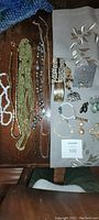 Overview of various strands of necklaces, bracelets, earrings, and brooches placed on a table and mat, showing colors and types of pieces included in the lot.