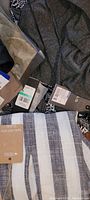 Photo showing various ladies clothing items with new tags including a gray knit top, striped fabric item, and patterned black and white garments
