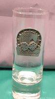Close-up of clear glass shot glass with metallic Las Vegas themed emblem featuring dice and slot machine motifs