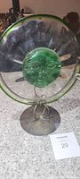 Front view of one Mexican green blown glass candle holder showing the circular glass disc with a raised face design at the center and green rim, mounted on a metal stand.