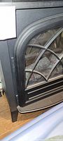 Close-up of black electric fireplace heater showing curved decorative grid on glass front and textured black metal housing.