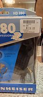 Close-up of headphone box corner showing model HD 280, pricing sticker, and brand name Sennheiser branding on clear packaging.