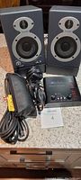 Pair of M-Audio studio monitor speakers, ART Tube MP preamp, microphone cable, and carrying pouch on countertop.