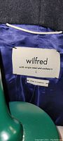 Close-up of Wilfred brand label showing 'with virgin wool and cashmere' and size L tag inside the coat.