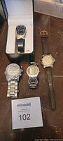 Lot of five watches displayed on wooden surface, one in original box