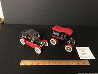 Two vintage ERTL toy bank trucks side by side with a ruler for scale, showing black and red paint and advertising decals. Both are approximately 5 inches long.