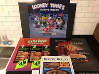 Four McDonald's promotional signs from the 1990s displayed on a table, featuring Looney Tunes plush toy offer, McRib combo, deluxe sandwiches, and pizza combos.