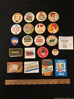 Full lot of 20 enamel and button-style McDonald's employee pins laid out in rows on a black cloth backdrop, with a ruler for scale.