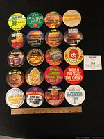 Top-down photo showing all 20 round employee pins arranged in 4 rows on a white background with ruler for scale.