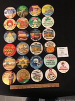 Photo of 25 McDonald's employee promotional pins arranged in rows on dark background with seller lot number card and ruler for scale.