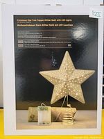 Photo of the boxed gold star Christmas tree topper showing star shape, LED lights, spring base, and product info on packaging.