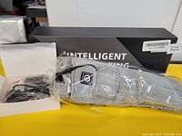 Grey intelligent heated socks packaged in plastic with a charger and electrical cables, placed next to a black box labeled 'Intelligent Heating'.