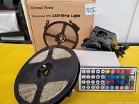 LED strip light on black reel, black power adapter, and remote control in front of product box labeled 'Eternal Home Waterproof IP65 LED Strip Light'.