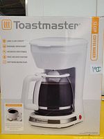 Front view of the Toastmaster coffee maker box showing an image of the coffee maker, highlighting features such as large 12 cup capacity, removable brew basket, integrated cord storage, pause and serve function, and keep warm heating plate.
