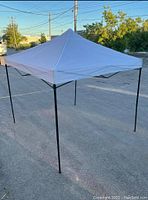 White pop up canopy tent fully set up outdoors on pavement showing black metal legs and white canopy top.