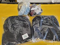 Photo showing two black knit toques individually packaged in plastic and two packs of fuzzy earmuffs (one light blue mix, one dark multicolored) on a yellow surface.