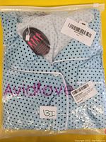 Pajama set neatly folded in packaging, showing light blue fabric with black polka dots and white piping, with brand tag Avidlove visible.