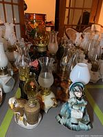 Overview photo showing diverse collection of oil lamps, some with animal and figurine bases and various glass chimney styles.