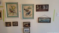 Wall display of seven framed art prints showing bird prints, landscapes, and seascapes